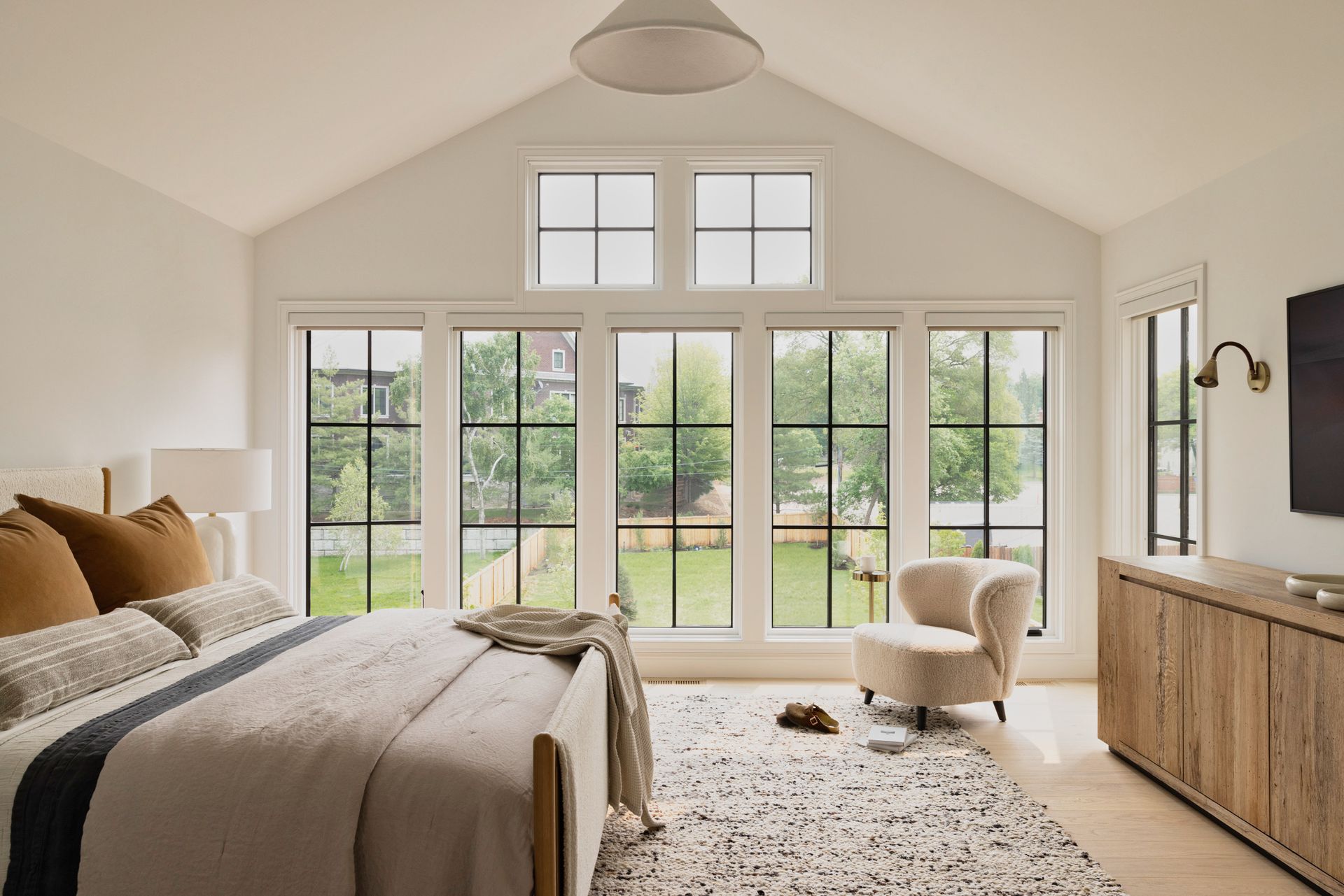 A bedroom with a bed , chair , television and lots of windows.
