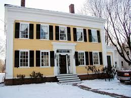 A large yellow house with black shutters is covered in snow.