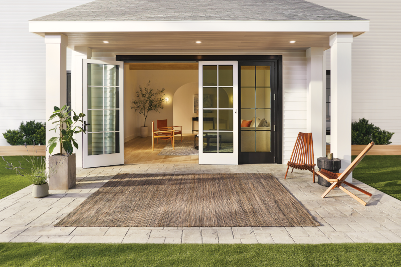 A patio with a rug and chairs in front of a house with sliding glass doors.