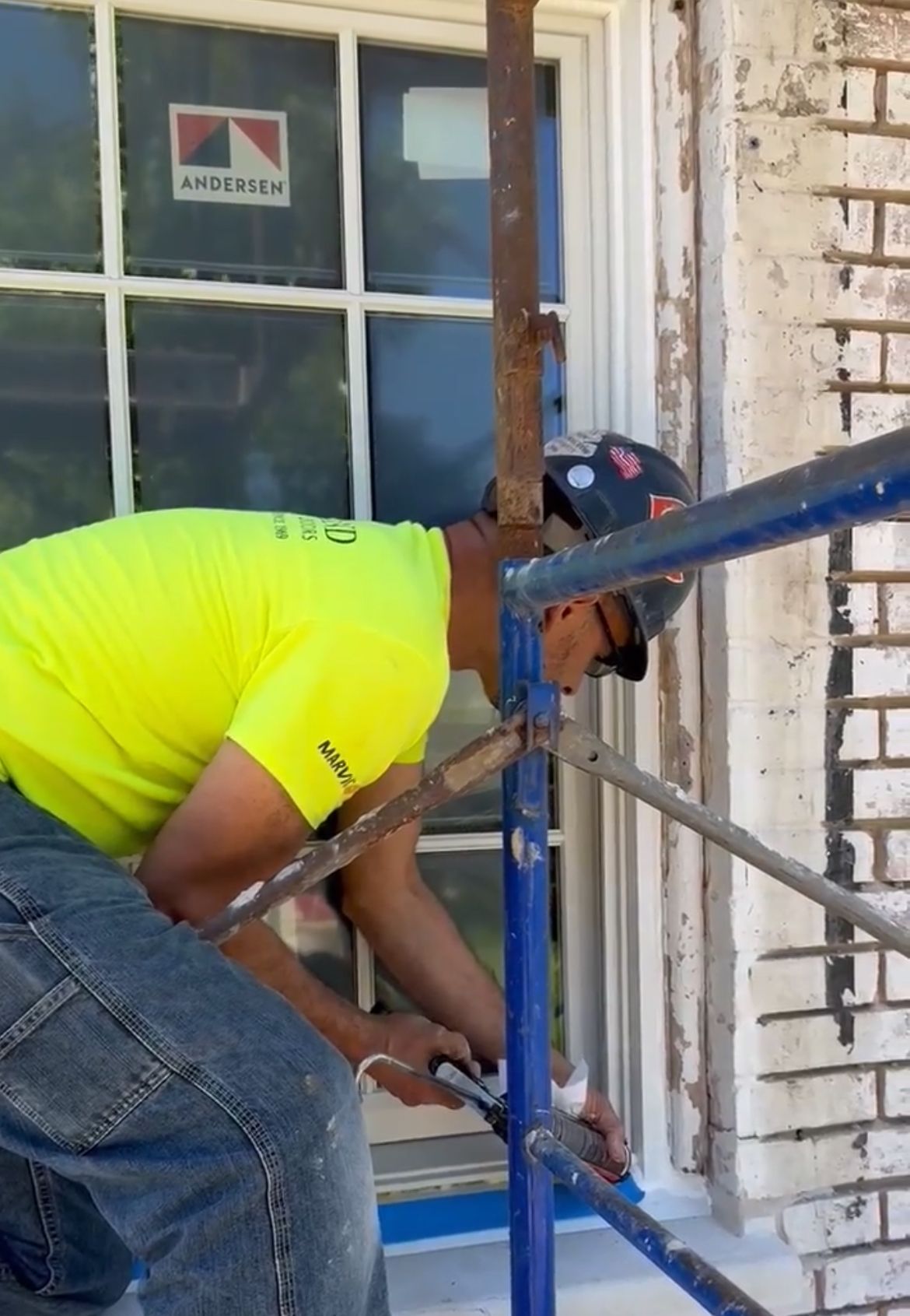 A man in a yellow shirt is working on a window