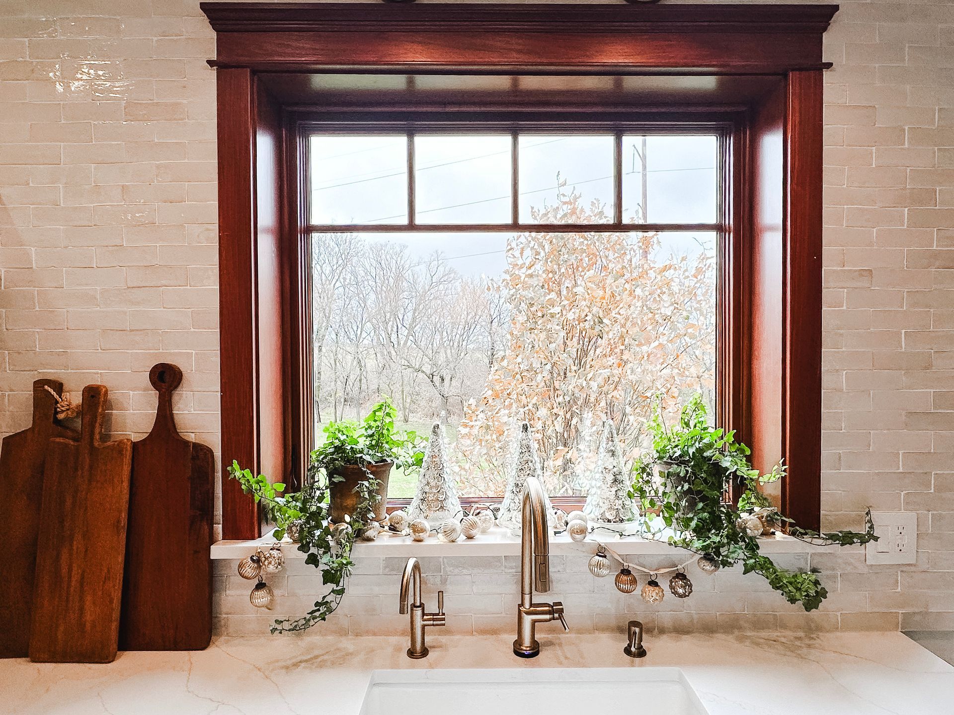 A kitchen sink with a window over it and cutting boards on the counter.