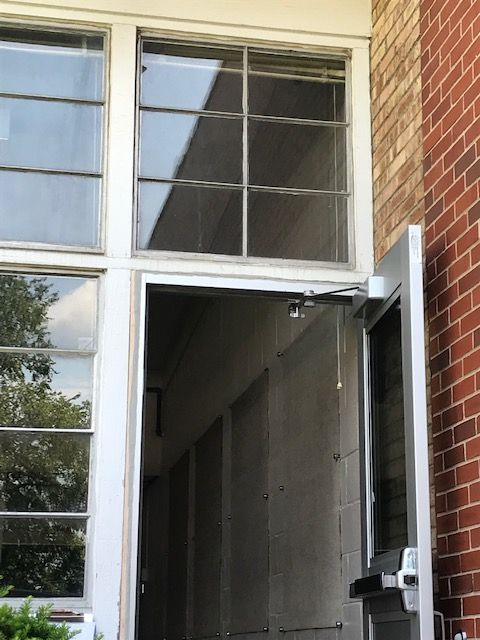 White doorway with glass window and brick wall; automatic door opener visible.