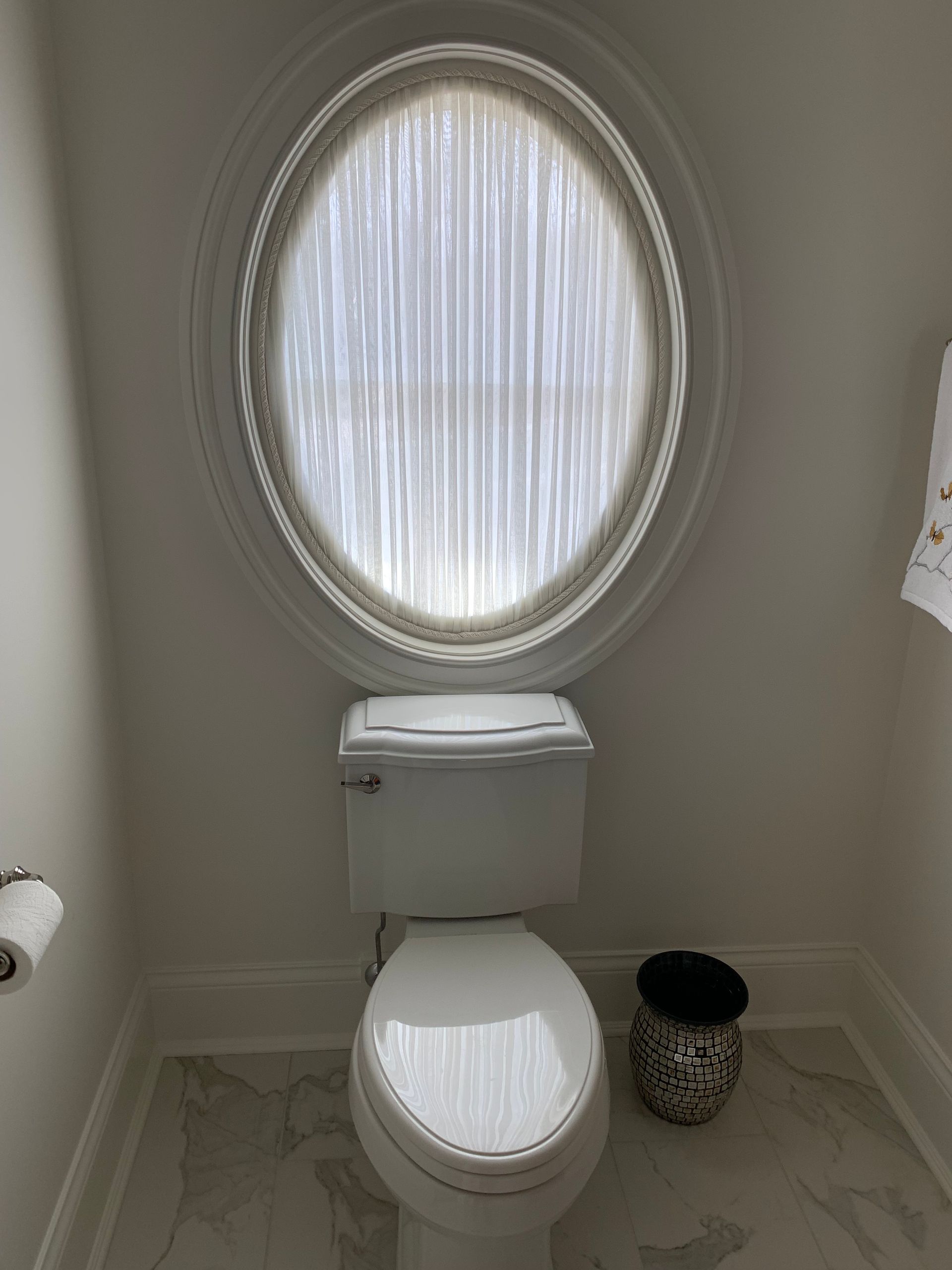 Toilet in bathroom with oval window above, and decorative jar to the right.
