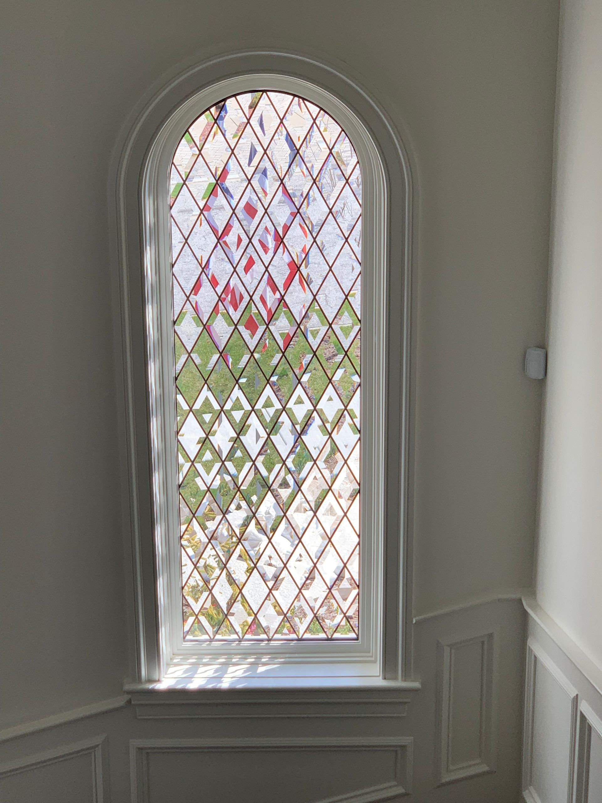 Arched window with diamond pattern glass. White trim. View of trees and sky through the glass.