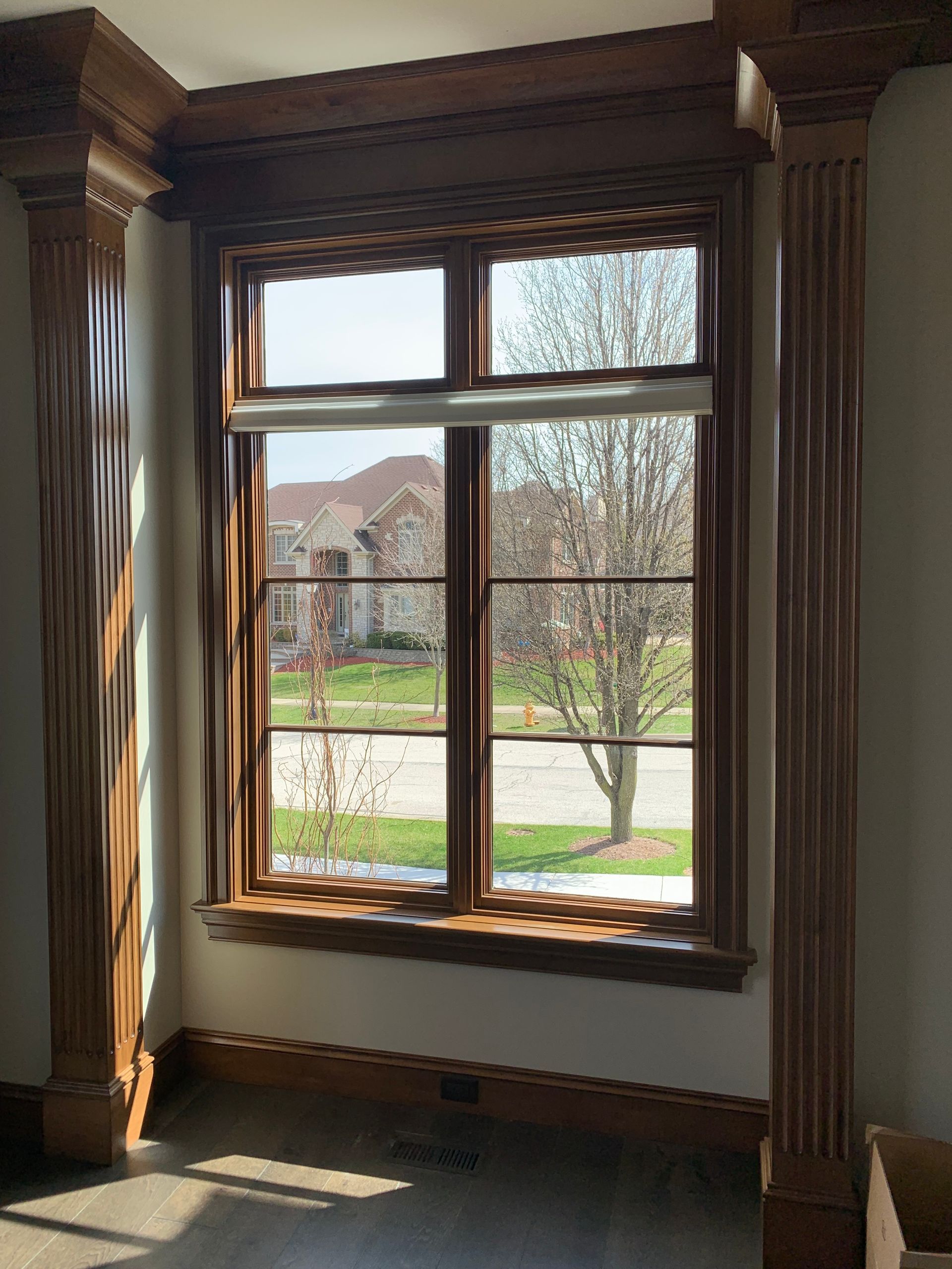 Window framed with wood trim and pillars, with a view of a house and trees outside.