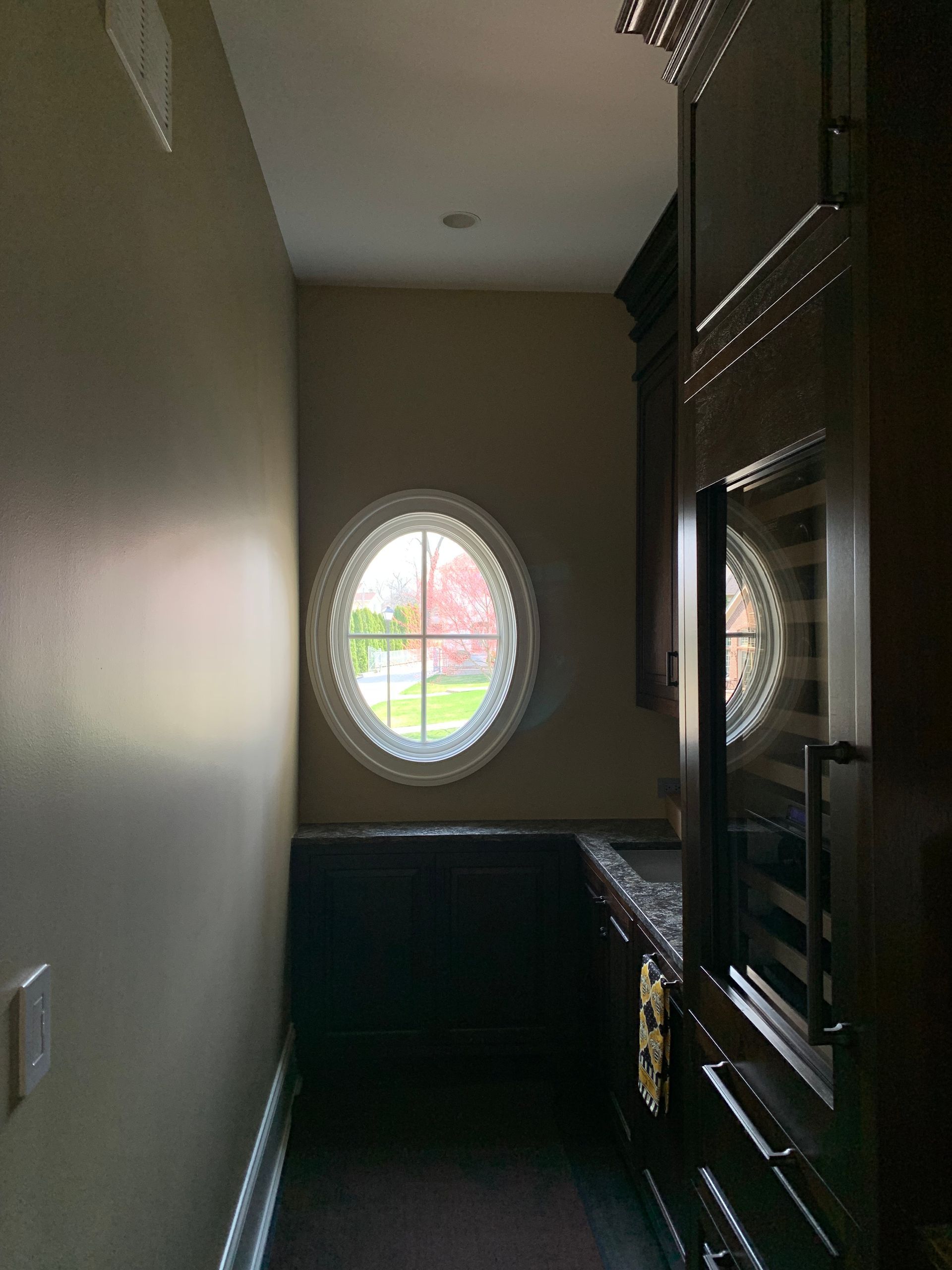 Narrow hallway with dark cabinets, oval windows with decorative trim, and a dark built-in appliance.