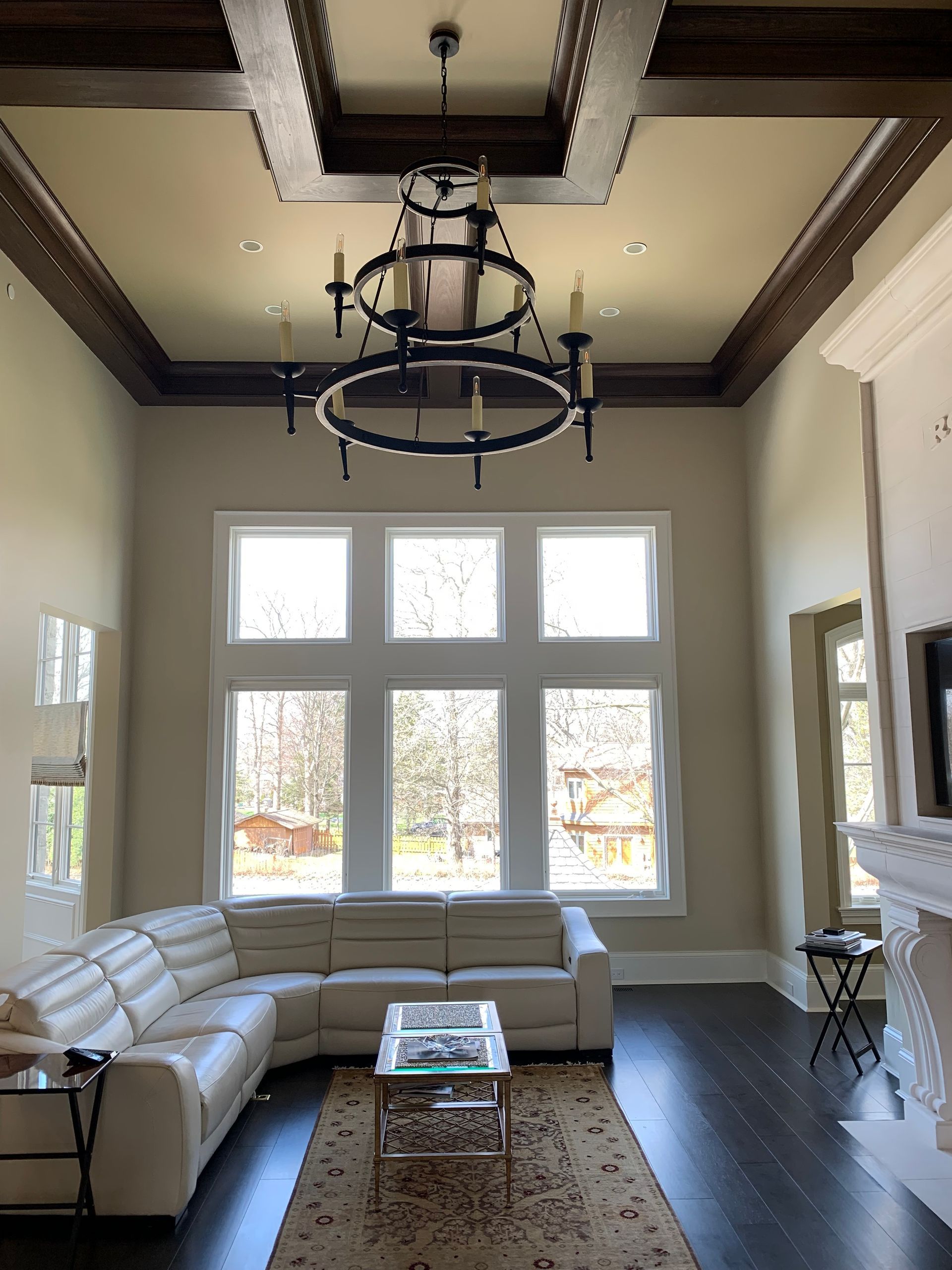 Living room with tall windows, chandelier, sectional sofa, dark wood floor, and coffered ceiling.