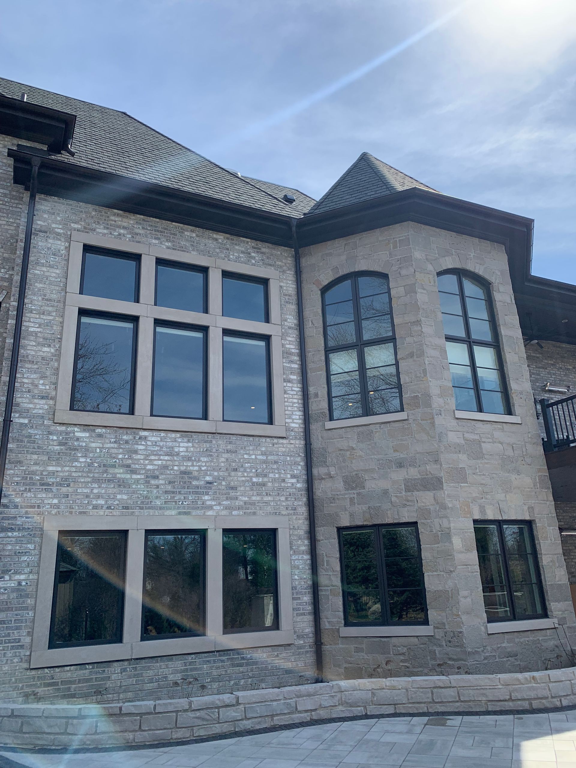 Two-story stone house with black-framed windows and a turret, under a bright blue sky.