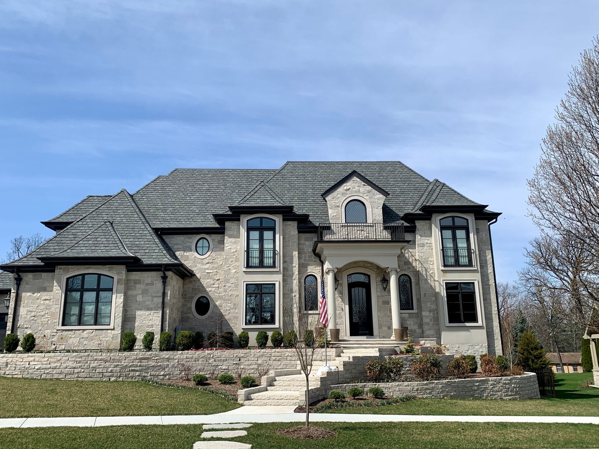 Large stone house with multiple stories, black-trimmed windows, gray roof, and a small American flag.