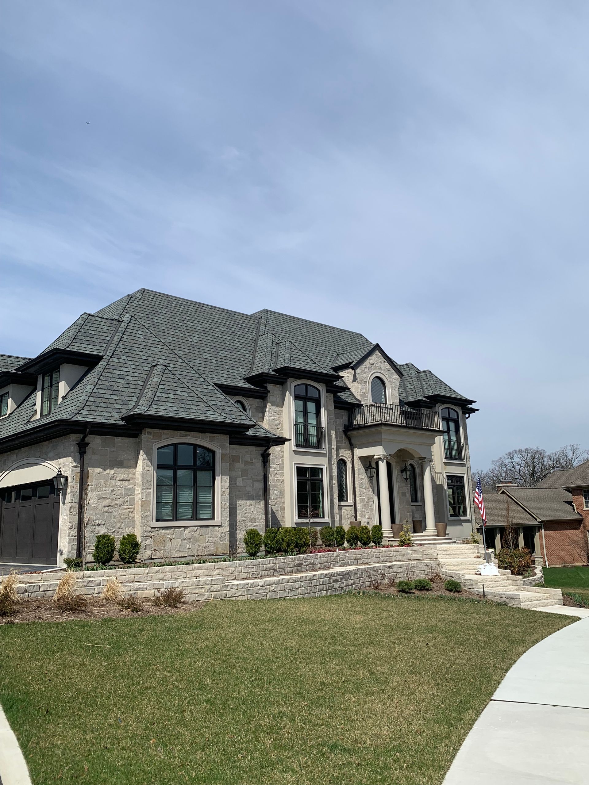 Large two-story brick house with a gray roof and black-trimmed windows, on a landscaped lawn.