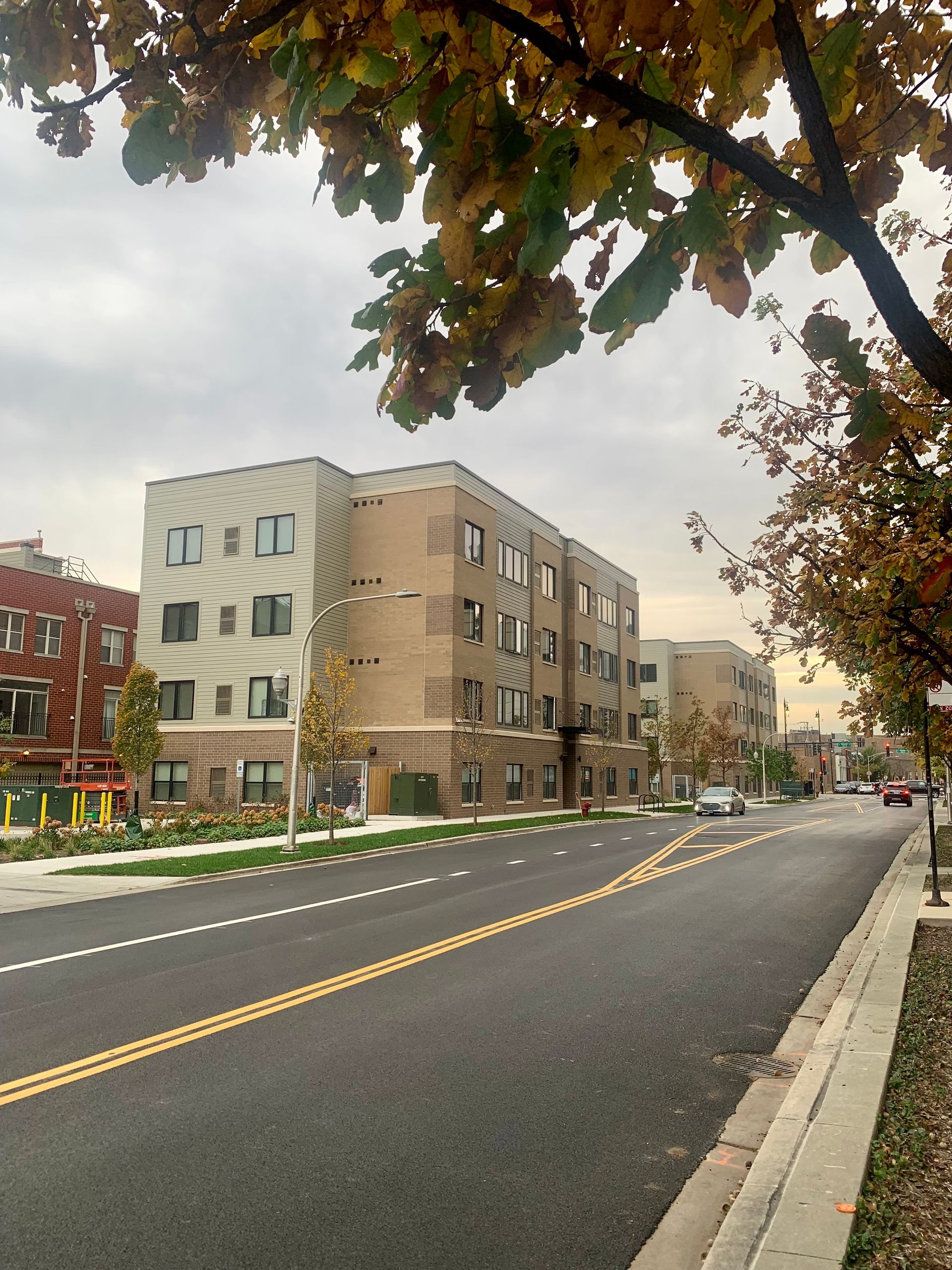 A multi-story apartment building on a city street with autumn leaves. Cloudy sky.
