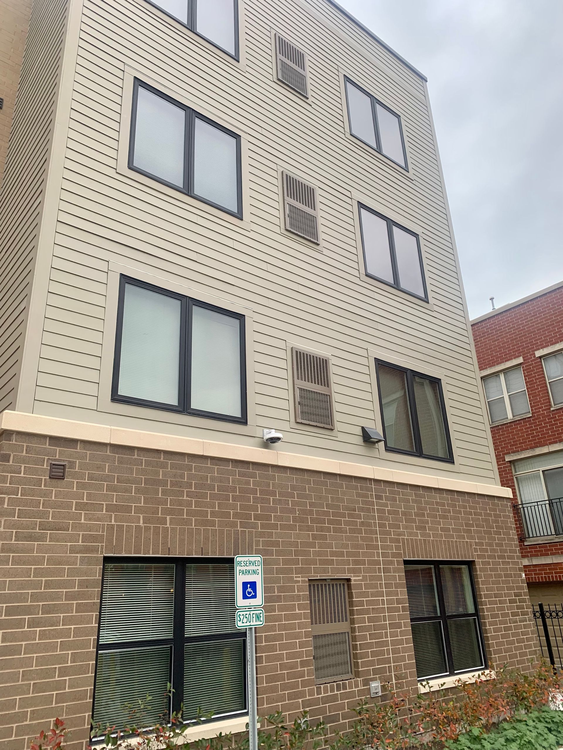 Multi-story building with brick base and tan siding, windows, and a handicap parking sign.