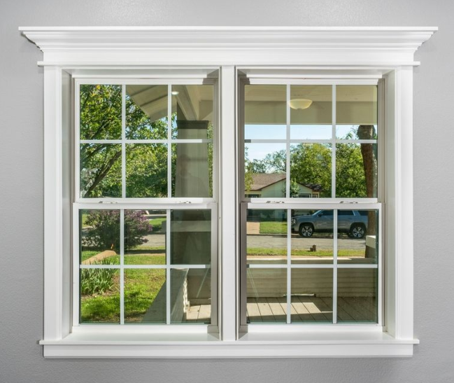 A white, double-hung window with a grid pattern, set into a plain grey wall, showing an outdoor neighborhood view.