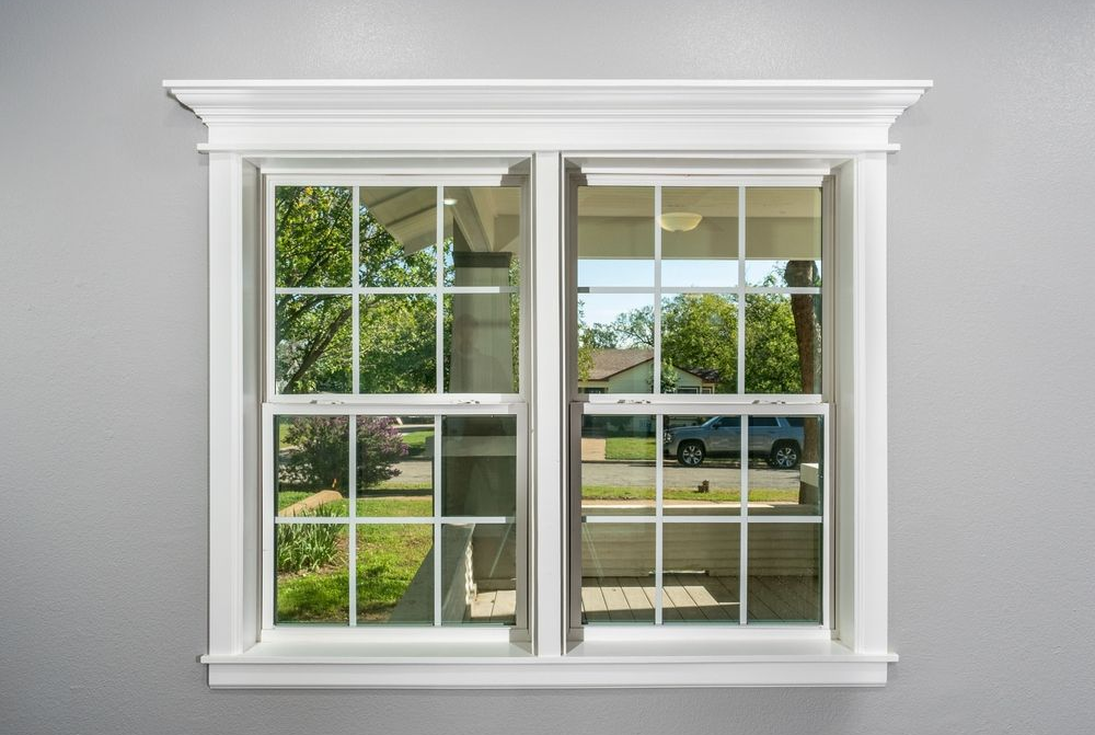 A white-framed, double-hung window with a grid pattern, showing a view of a porch, trees, and a car outside.