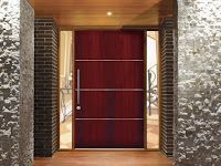 A red door with a stainless steel handle is in a hallway next to a brick wall.