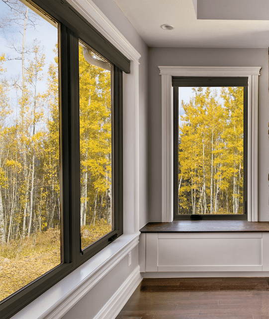 A room with two windows and a bench with a view of a forest.