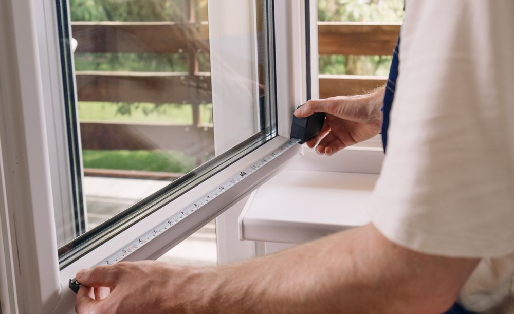 A person uses a tape measure to check the dimensions of a white window frame.