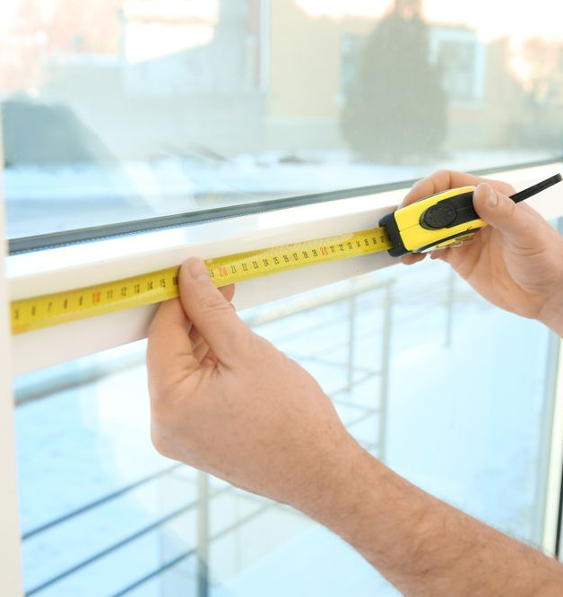 Hands measuring a white window frame with a yellow retractable tape measure.