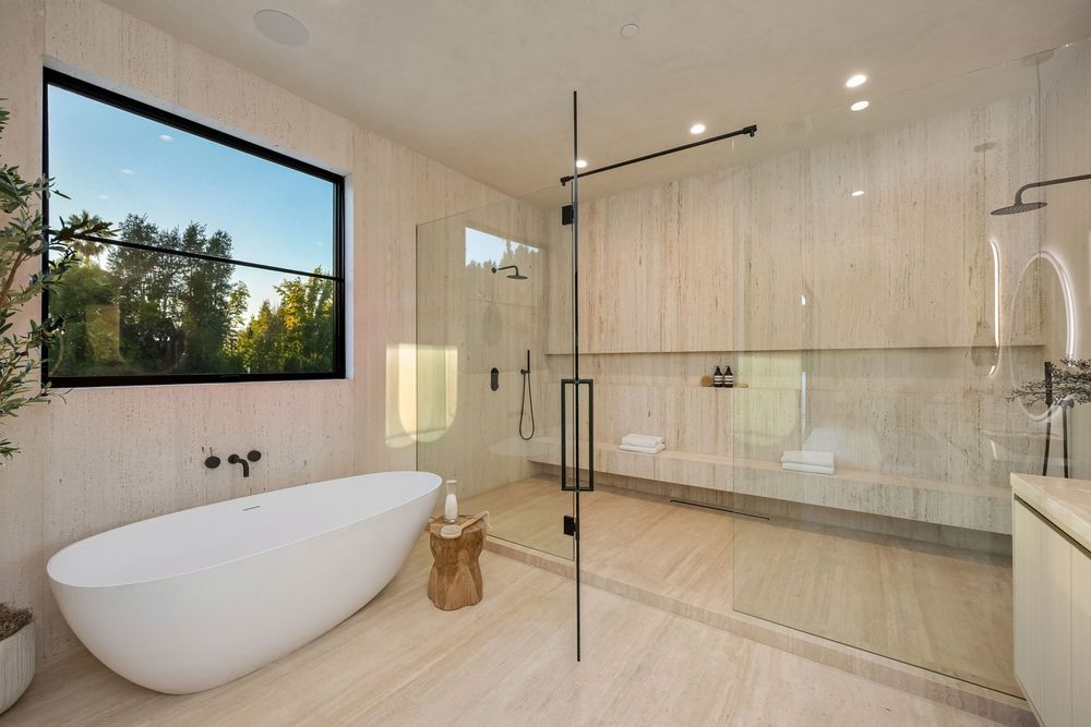 Modern bathroom with a soaking tub near a window, and a large glass shower.