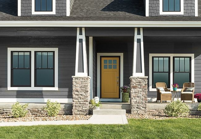 The front of a gray house with a yellow door and windows.