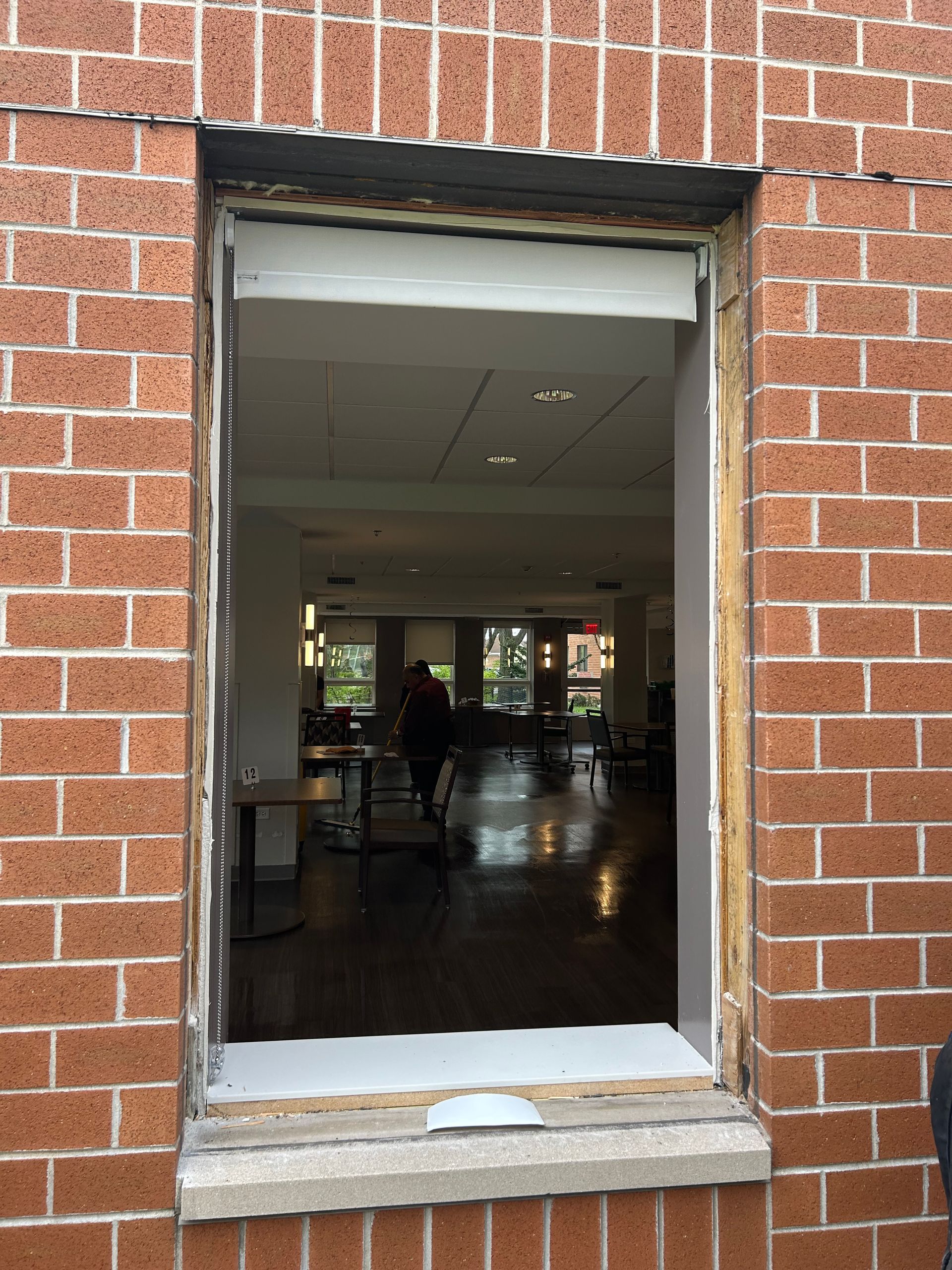 Exterior view through a rectangular window frame into a dining area with a person walking.