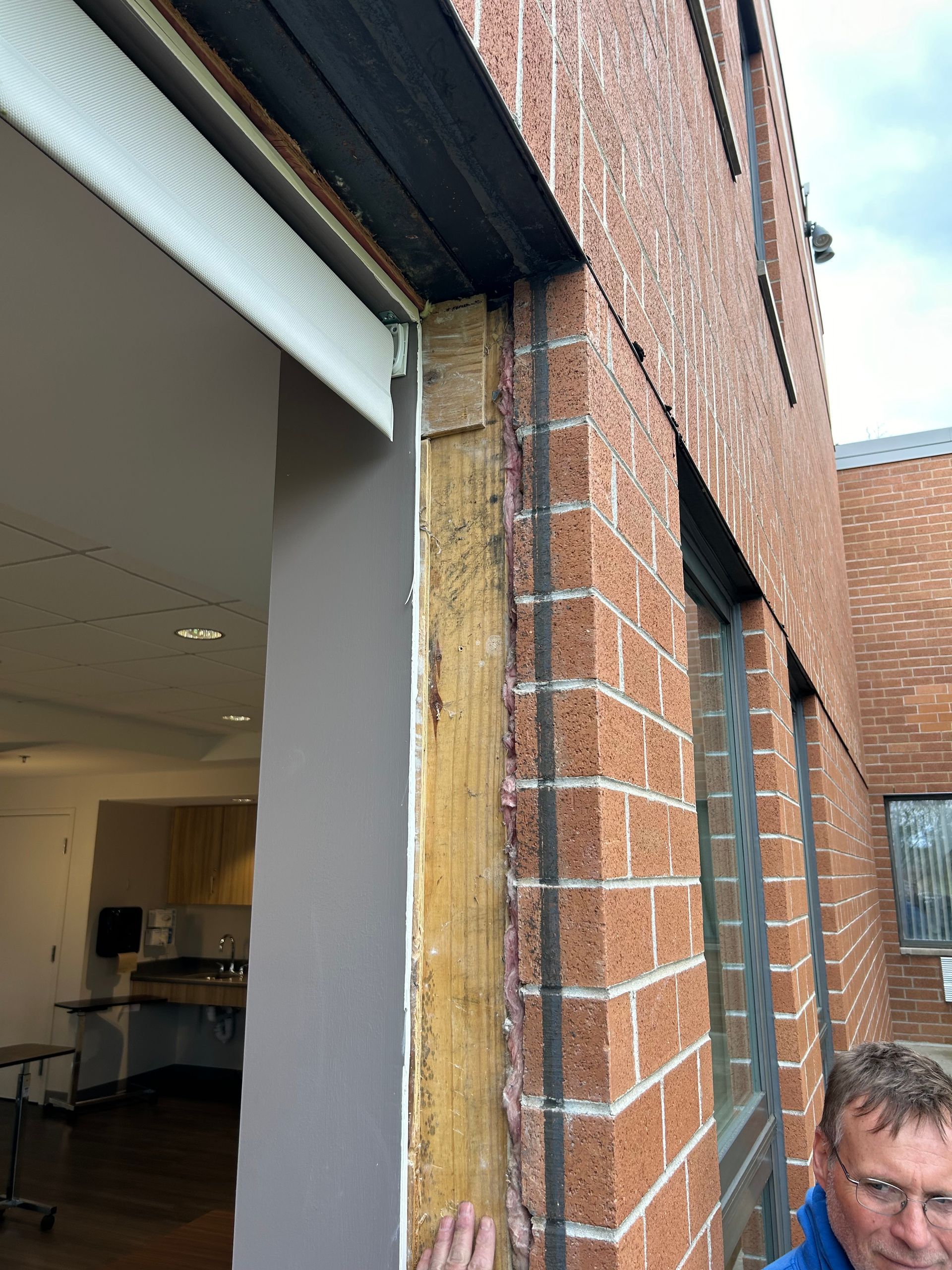 Exterior view of a brick building. Damaged wooden frame around a window opening. A person in the frame.