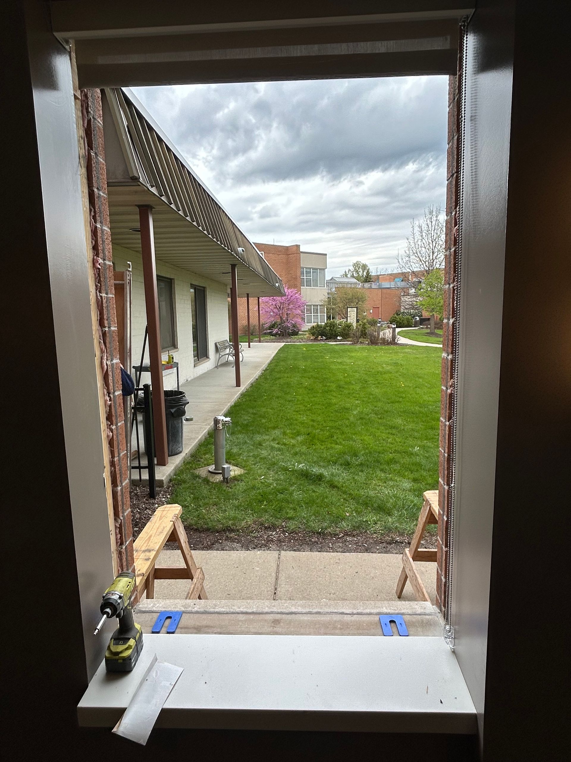 View from a window: a partially completed project, overlooking a green yard and buildings.