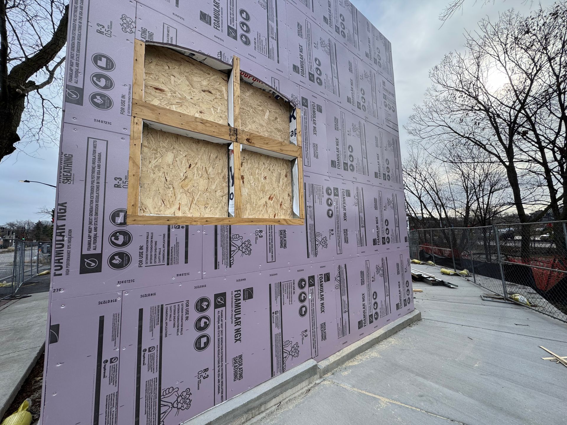 A building under construction with purple insulation panels and a boarded-up arched window frame.