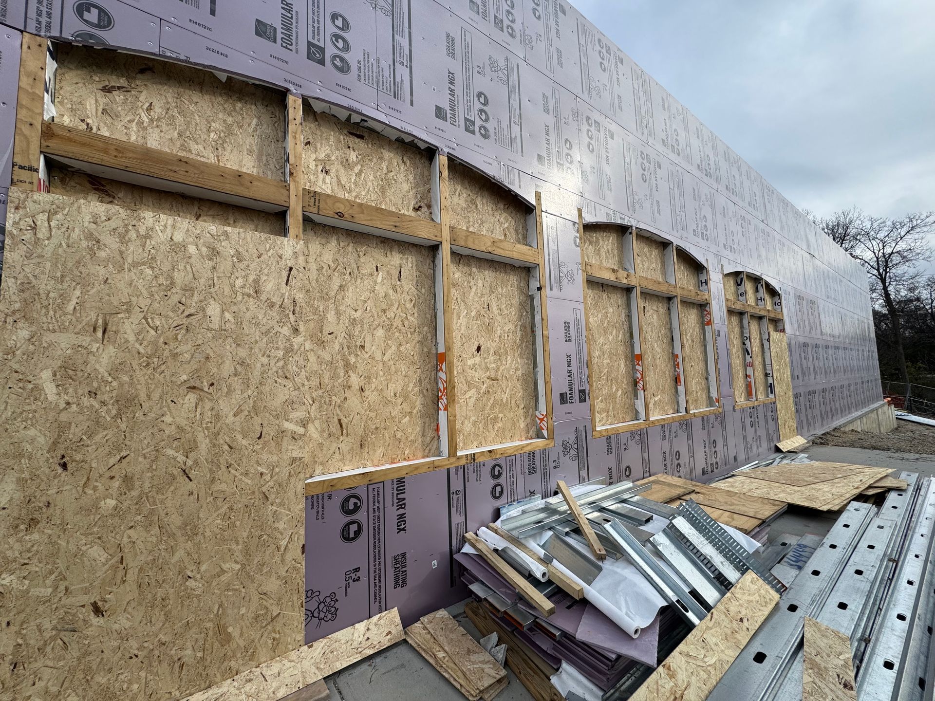 Construction site: exterior wall with arched window frames, OSB sheathing, and pink insulation.