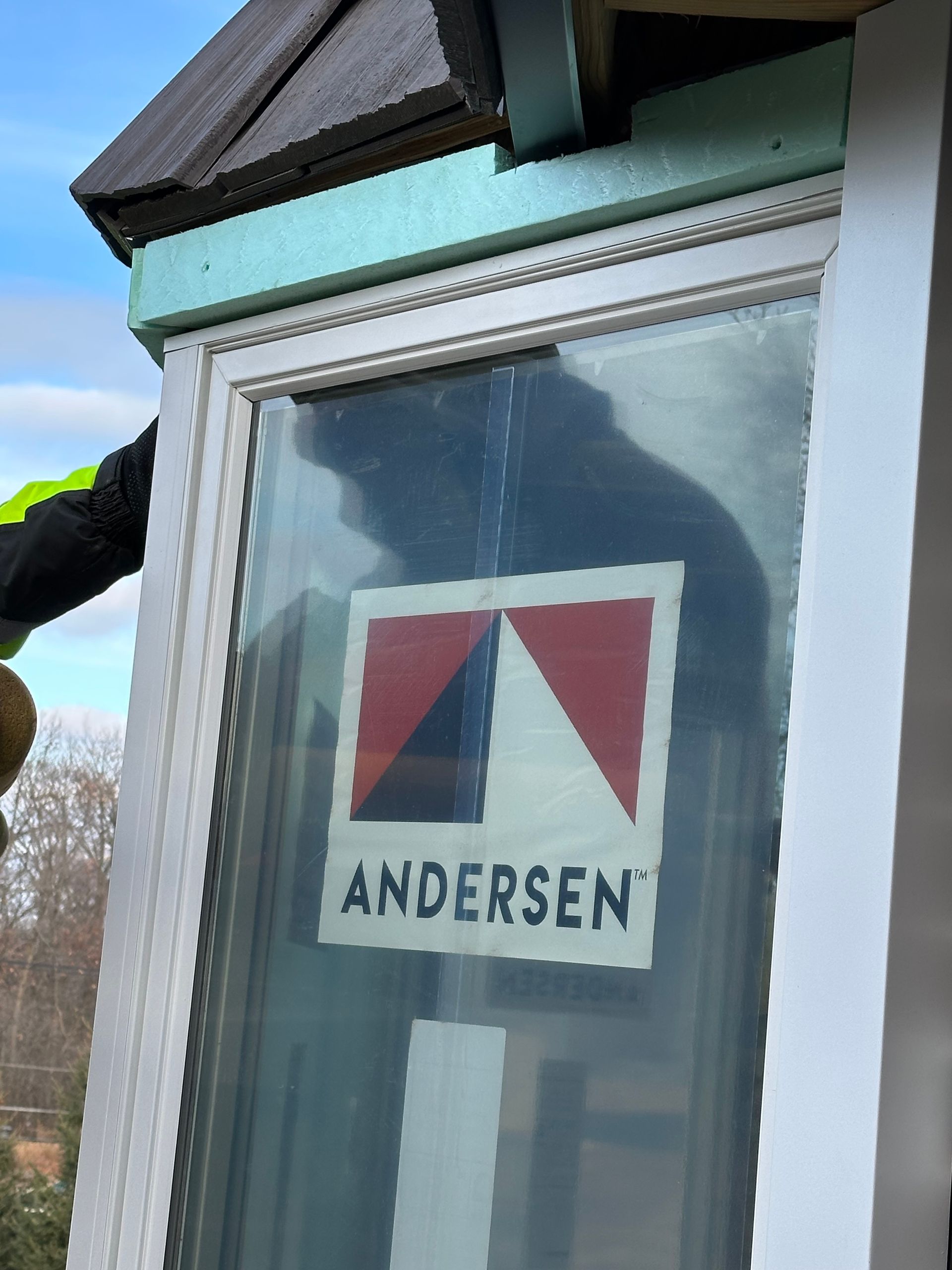 A worker installing an Andersen window. The window frame is white with a sticker. Blue insulation visible.