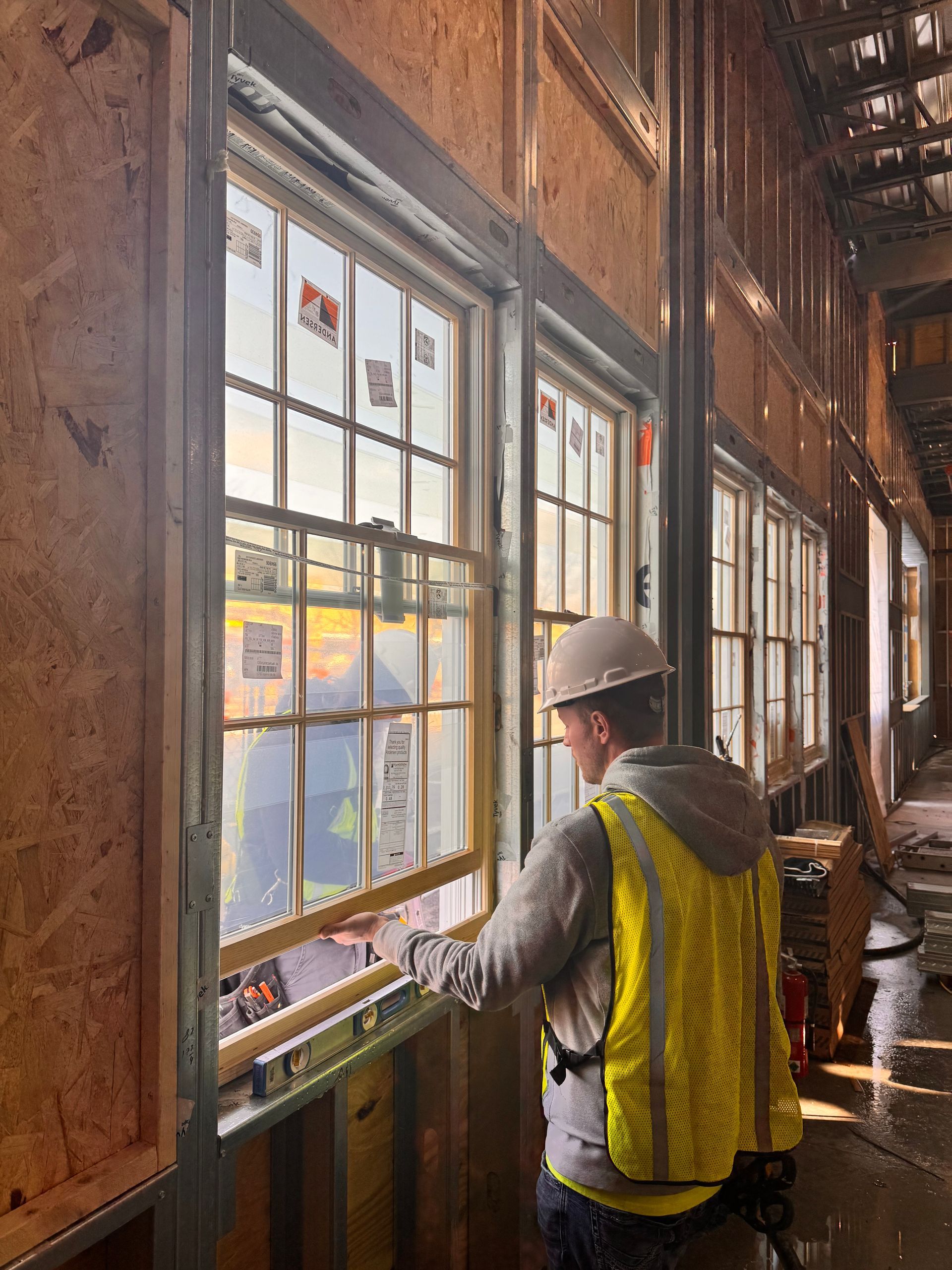 Construction worker examining a window in a building under construction; yellow safety vest, white hard hat.