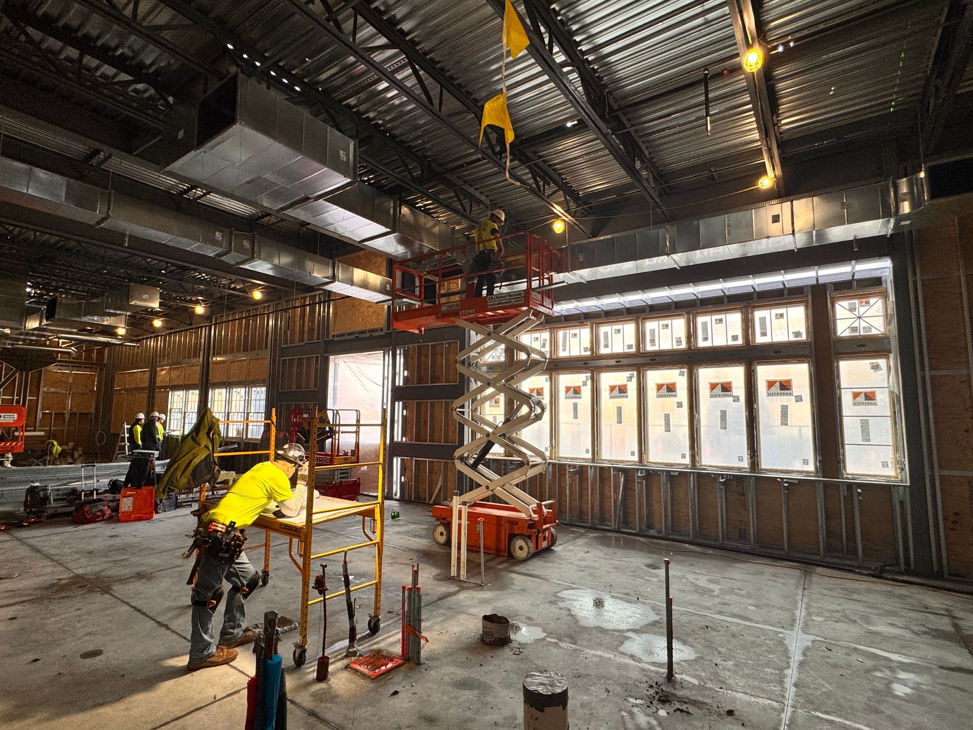 Construction site with workers, lift equipment, and a partially framed window wall.
