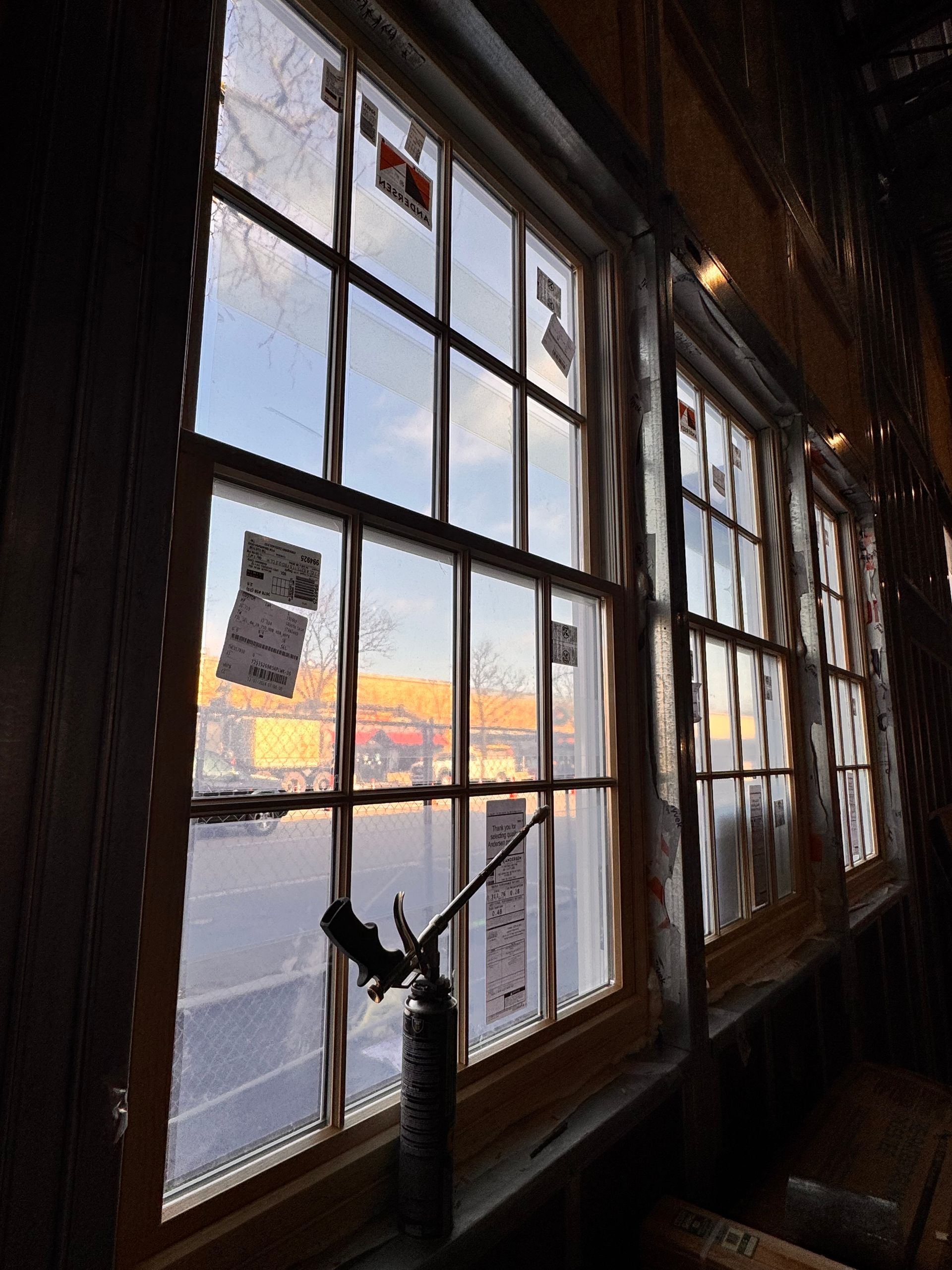 View through multi-paned windows at dusk; golden light reflects off distant buildings.