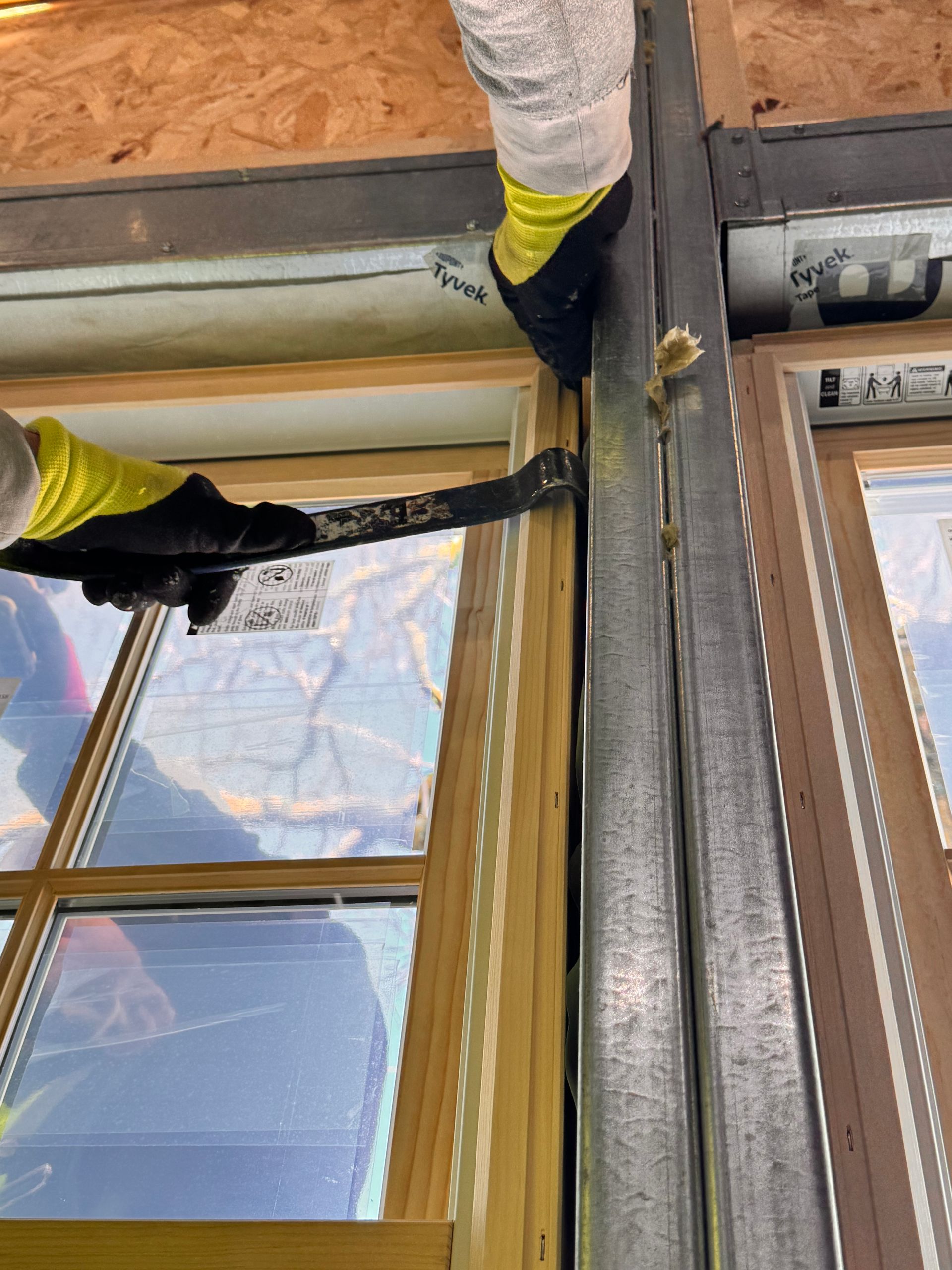 Person in gloves using a tool to pry at a window frame during construction.