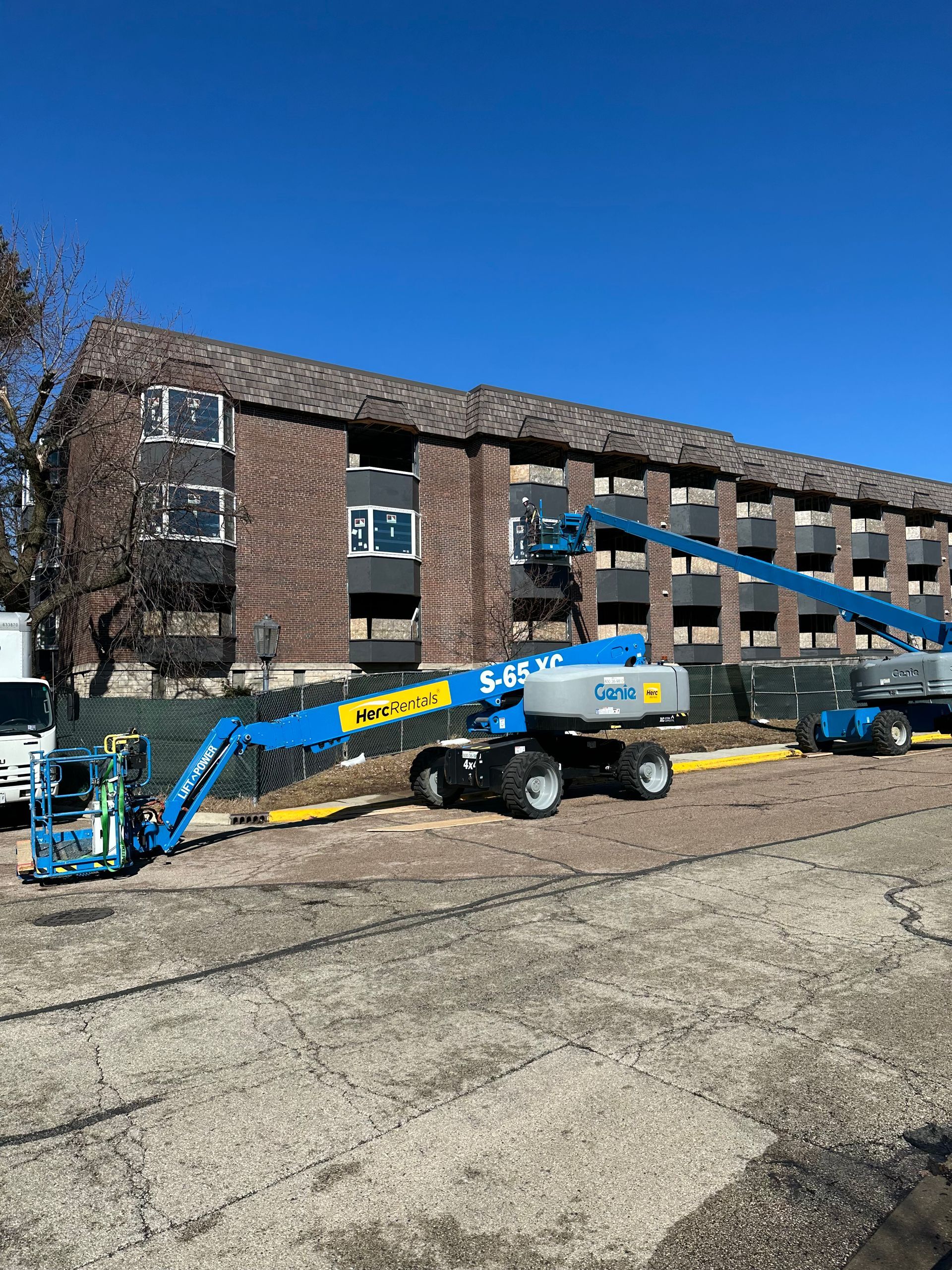 A blue construction lift in front of a multi-story brick building on a sunny day.