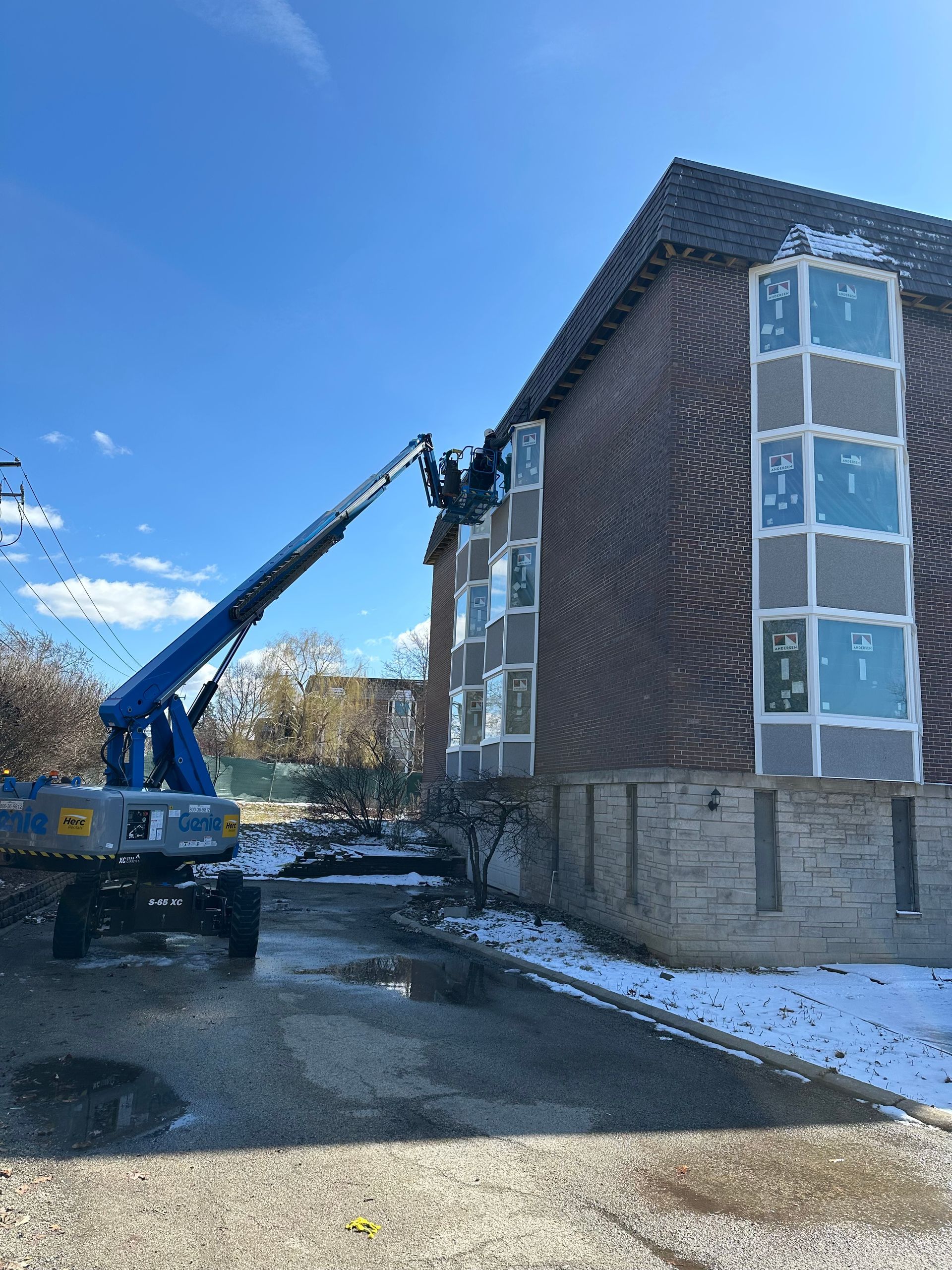 A blue boom lift working on the facade of a brick apartment building on a partly snowy day.