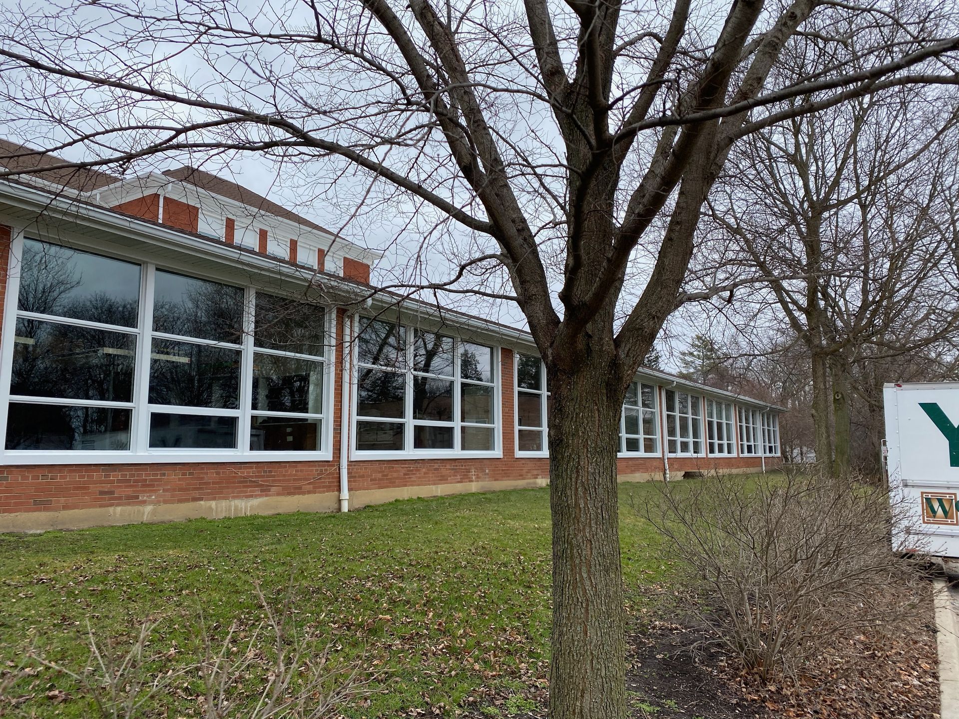 School building with large windows, brick, and bare trees on a cloudy day.