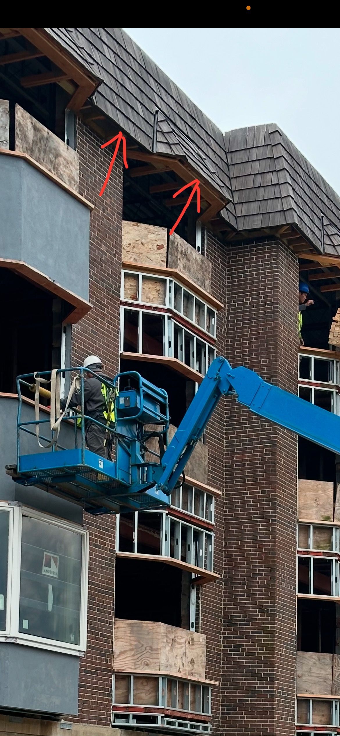 Construction worker in lift repairing building exterior with damaged roof.