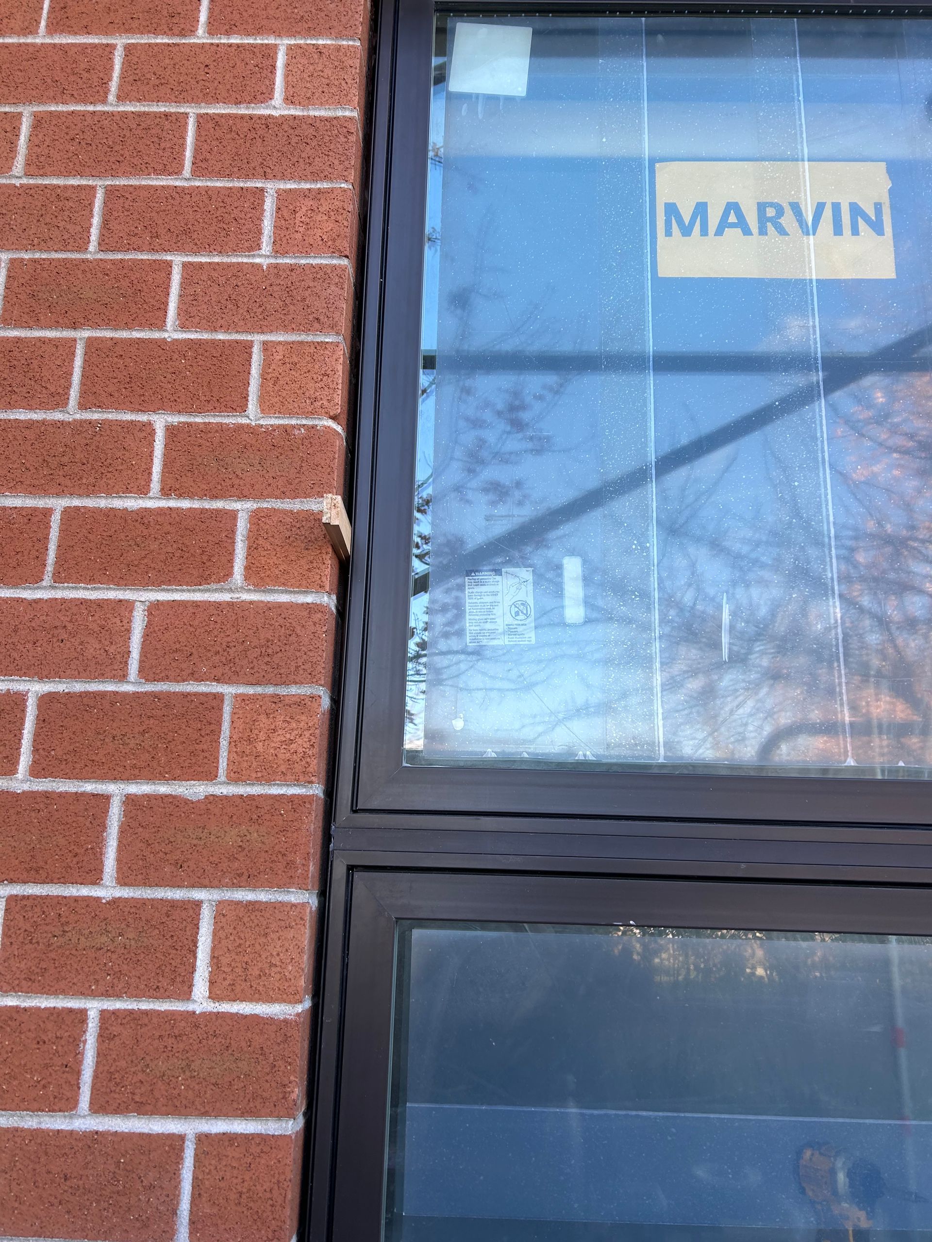 Brick wall next to a dark-framed window with a Marvin sticker.