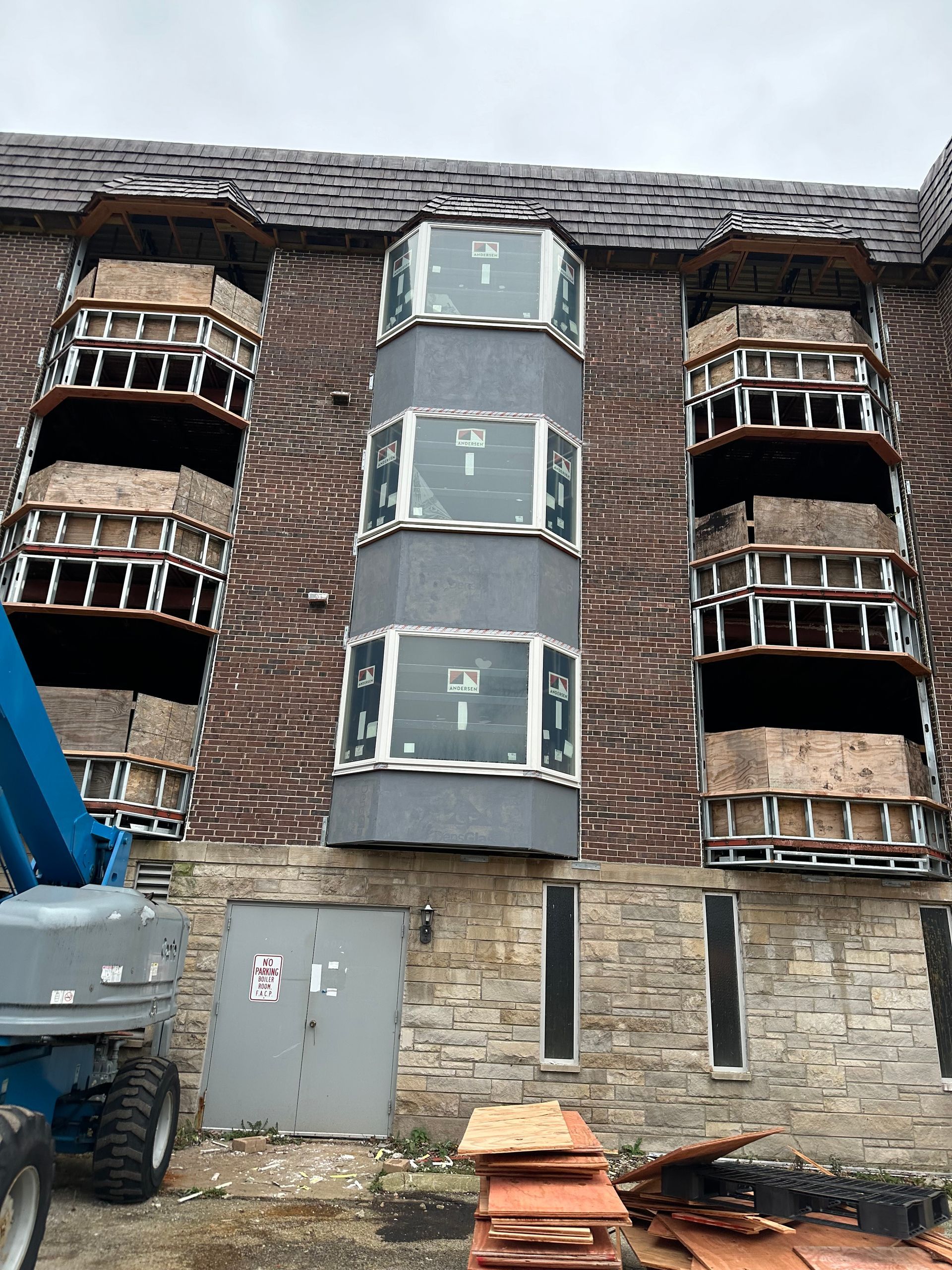 Building facade with three tower-like window sections under renovation. A lift is visible.