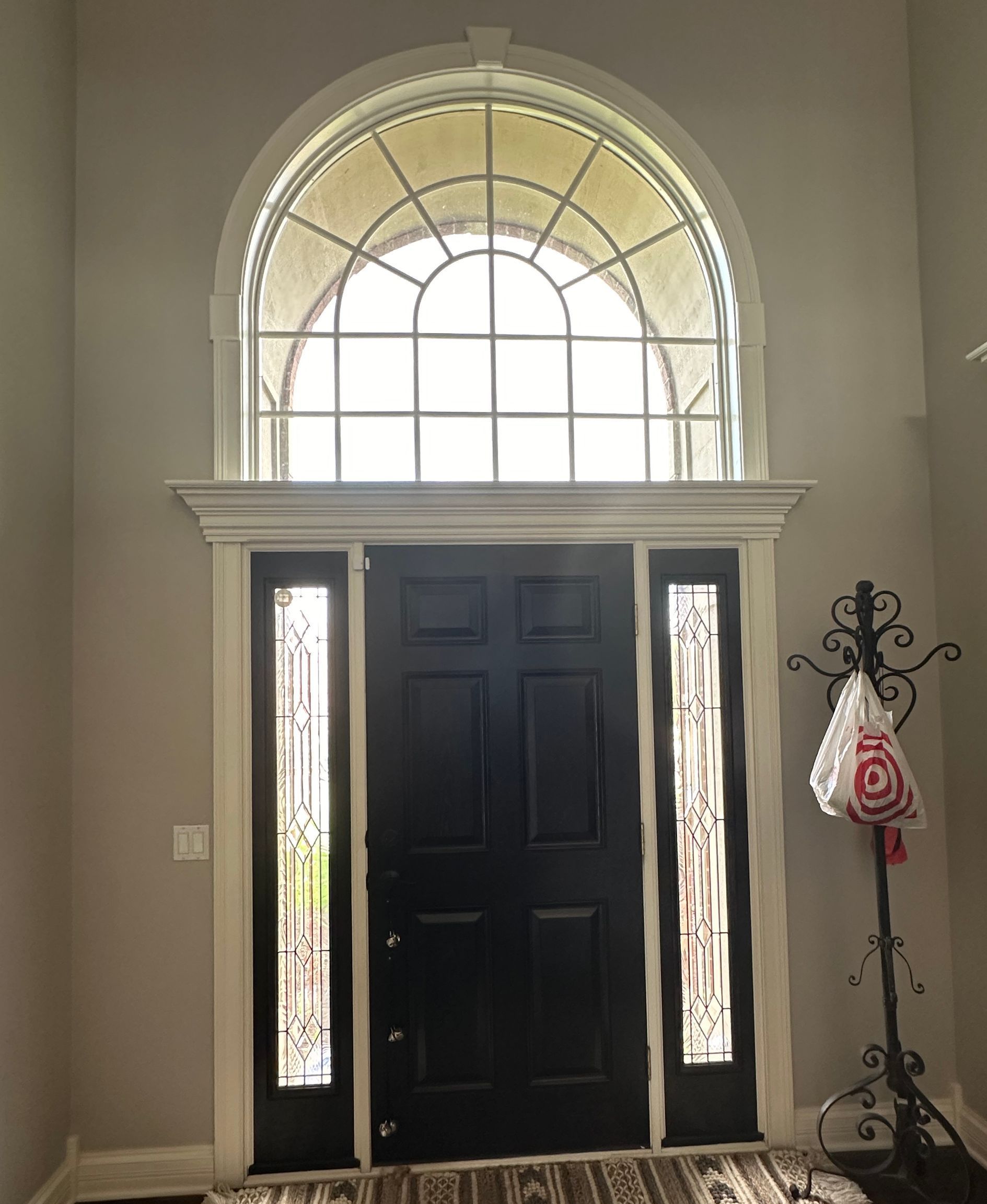 Black door with sidelights and arched window above, in a light-colored entry hall.