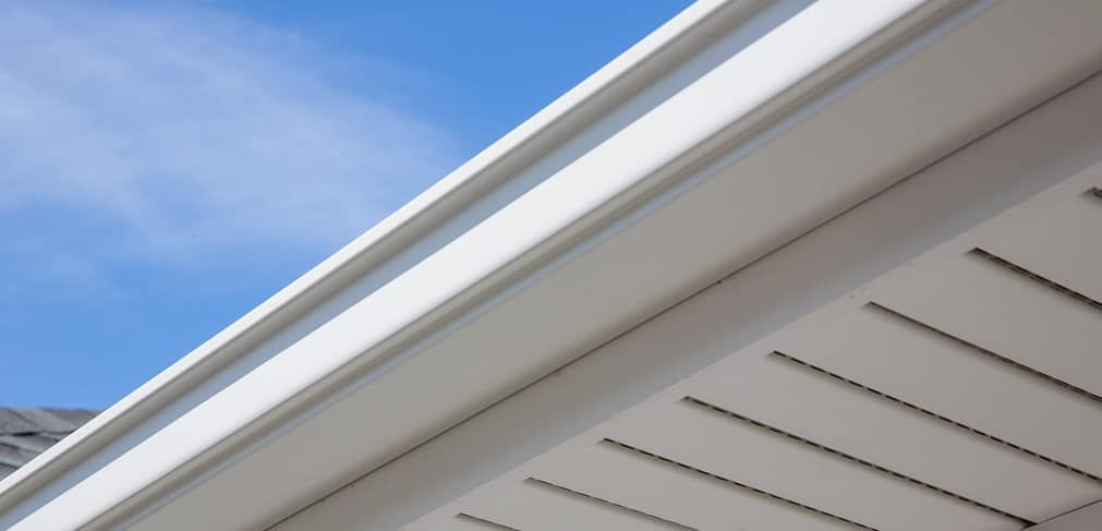 A close up of a white gutter on a house with a blue sky in the background.