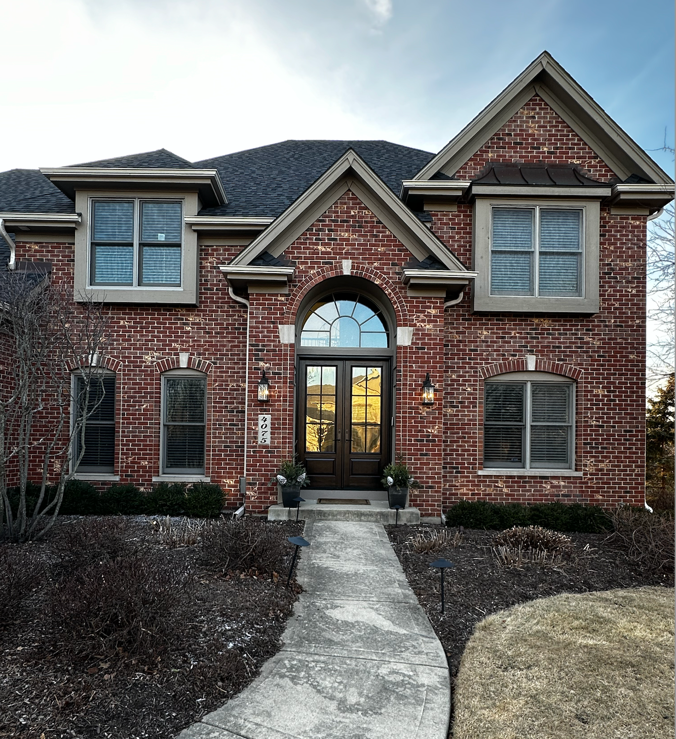 Brick house with arched door and shutters; pathway leads to entrance.