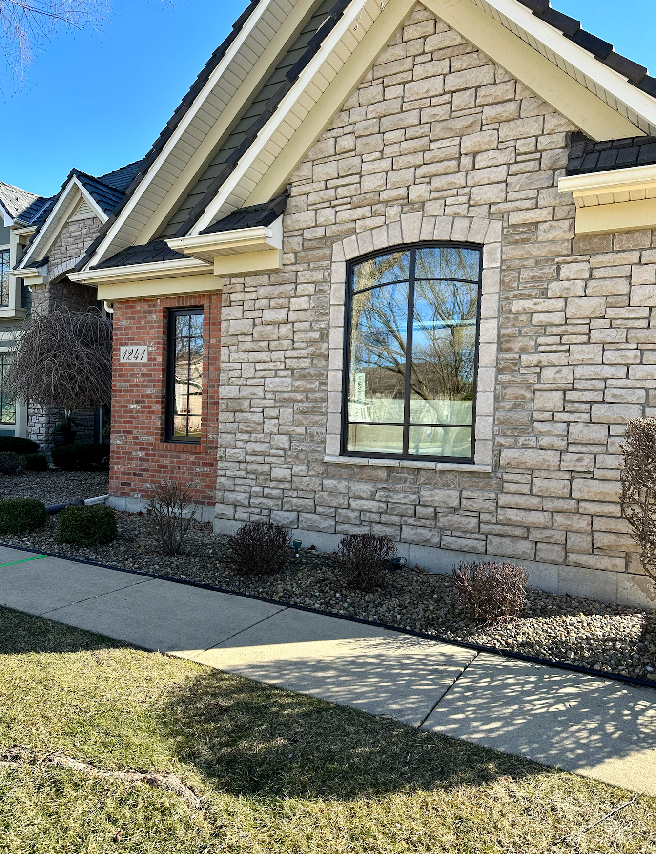 Stone house with a black framed arched window and a narrow rectangular window next to a brick wall.
