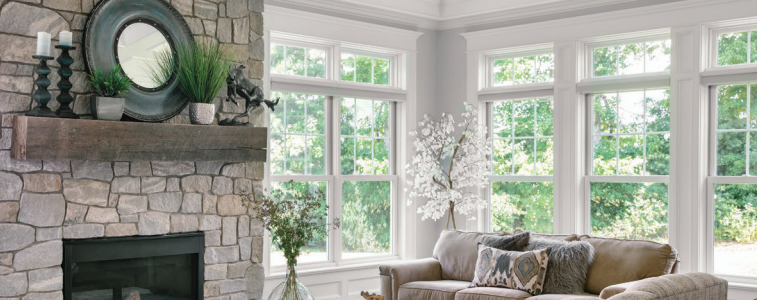 Gray study with large windows overlooking a green lawn, dark desk, built-in shelving, and tufted chair.
