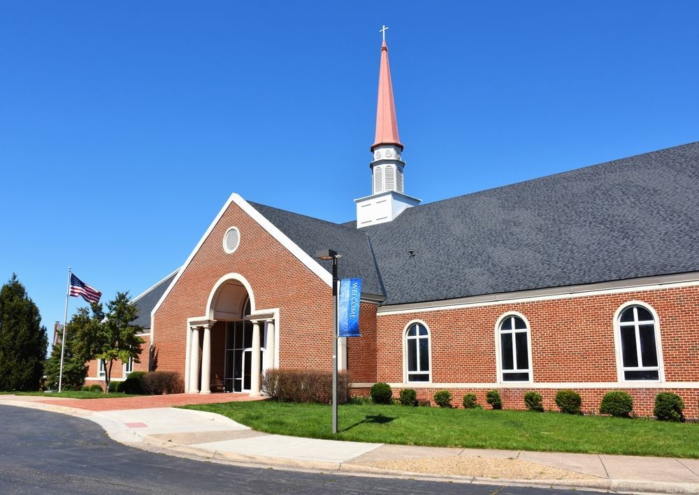 Brick church building with red steeple and blue sky.