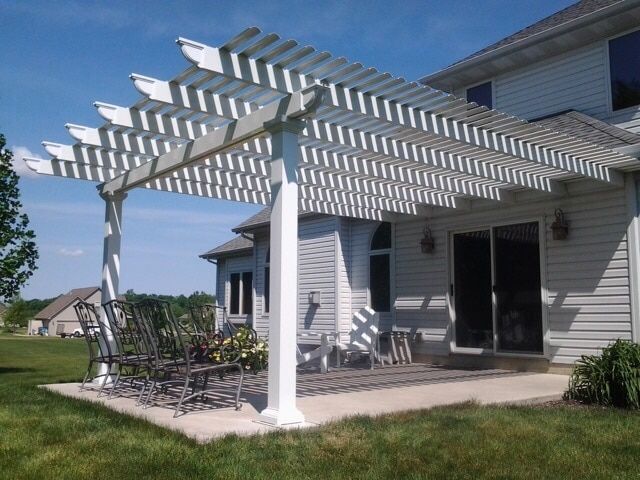 A white pergola is sitting on top of a patio in front of a house.