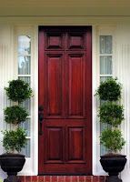 A red wooden door with potted plants in front of it.