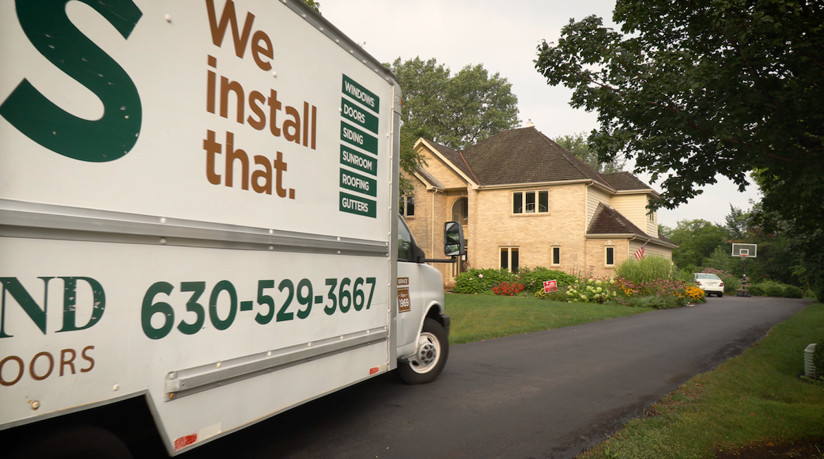 A white truck that says we install that is parked in front of a house.