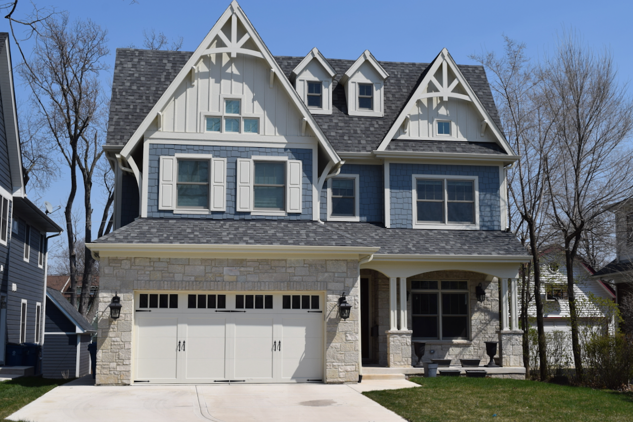 A large blue and white house with a gray roof and a white garage door.
